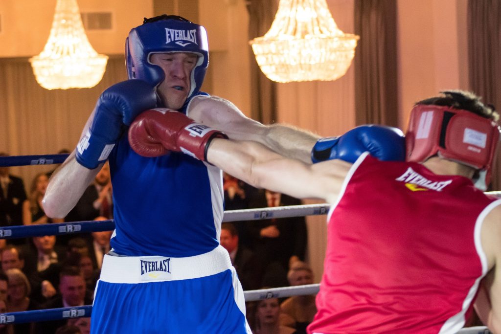 A boxer in blue (left) receives and delivers a punch to a boxer in red (right). 