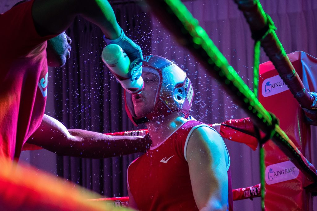 A trainer (left) splashes water from a bottle to his boxer in red (right). 