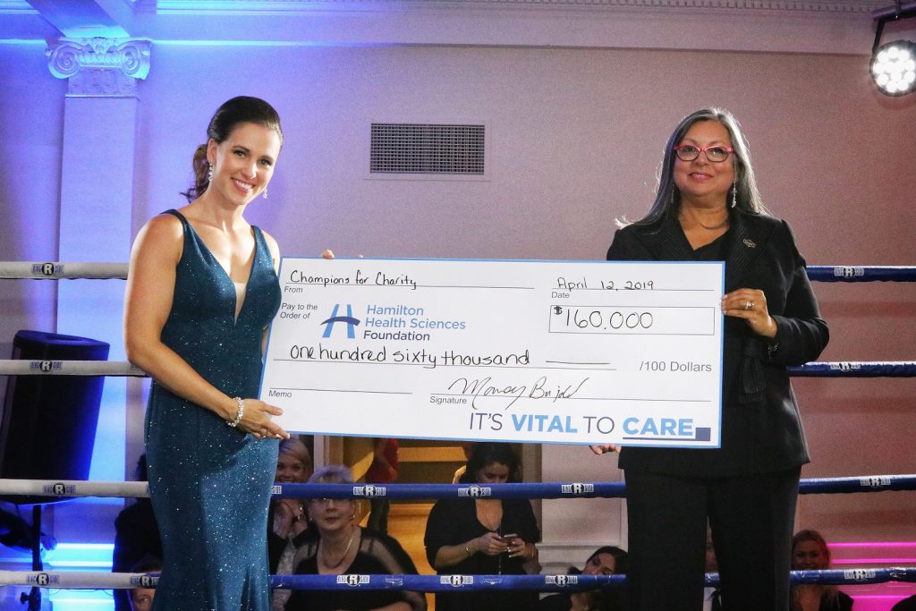 Mandy Bujold (left) holds a big cheque for $160,000 with Pearl Veenema (right). Both Mandy and Pearl are smiling in the boxing ring. 