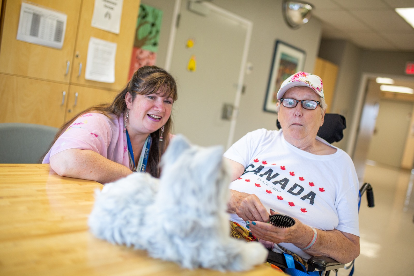 Therapeutic recreationist, Jean Riley, smiles a a patient makes funny faces at a grey robotic cat