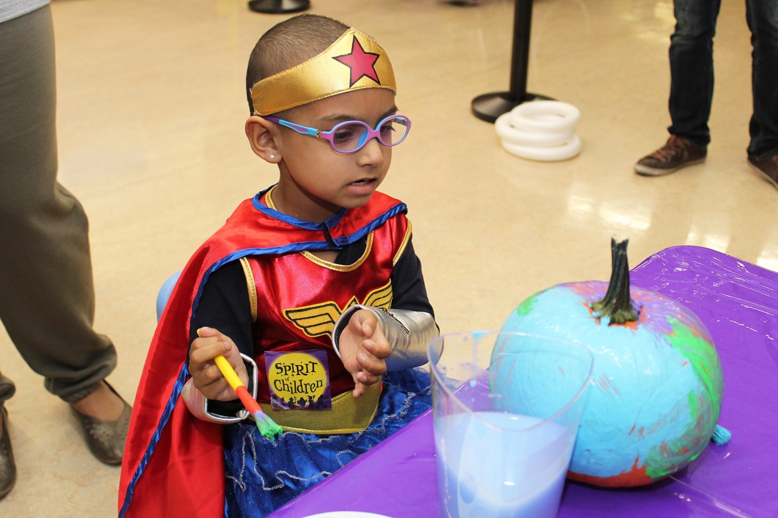 A MCH patient dressed as Wonder Woman is painting a pumpkin. 