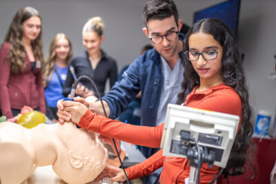 Dr. Connor Pepper, anesthesia resident at McMaster University teaches high school students how to intubate (place a breathing tube in the trachea) in a mannequin using a video laryngoscope.