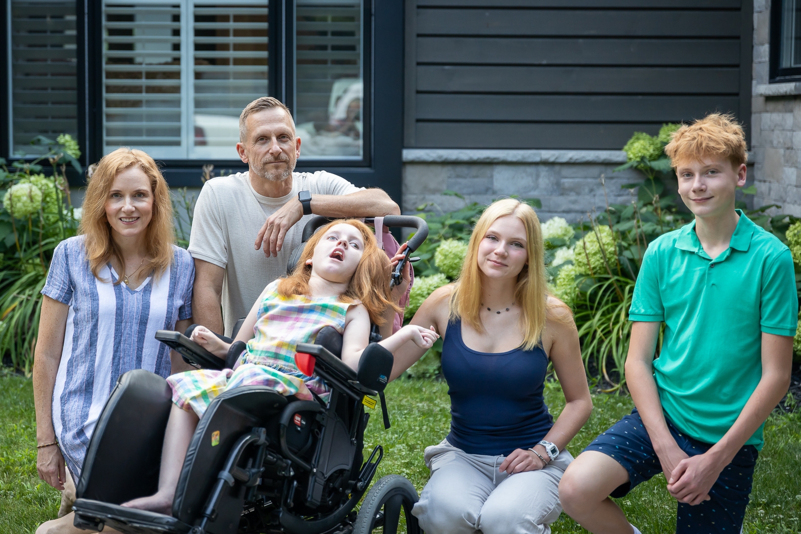 A family of five sits together in their garden. One child uses a wheelchair.