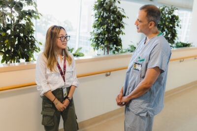 Grade 12 graduate Charis Cui stands in a hospital hallway with Dr. Pablo Serrano talking about her internship experience.