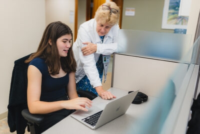 Grade 12 student Katherine Birchenough sits in front of a laptop computer, while Dr. Alison Fox-Robichaud leans forward to look at the screen.